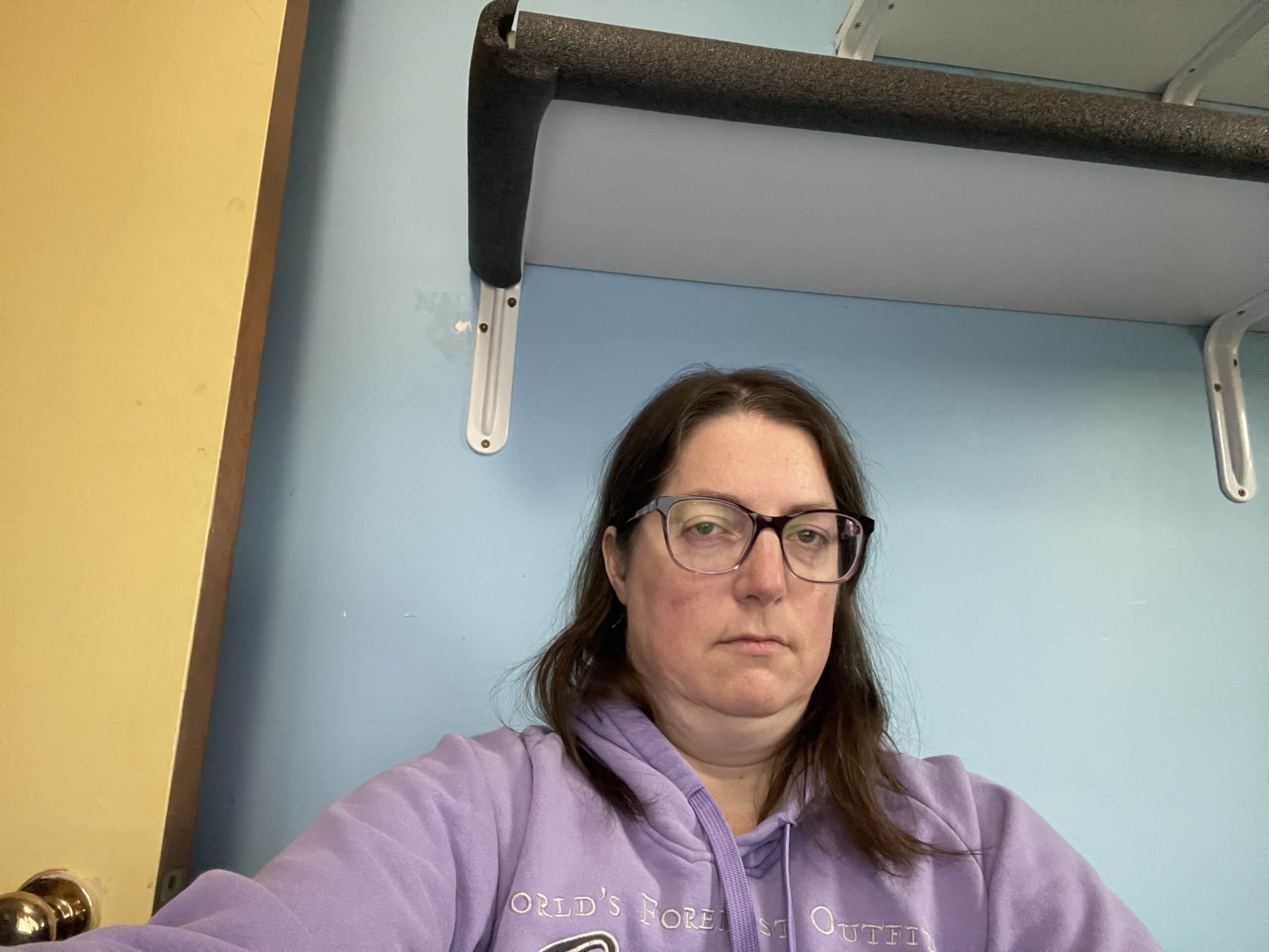 Woman wearing a purple sweatshirt looking unhappy.